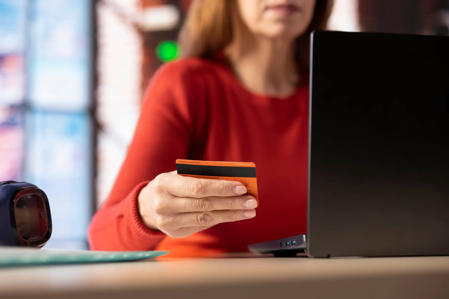 Femeie in pulover rosu facand o plata cu cardul la laptop